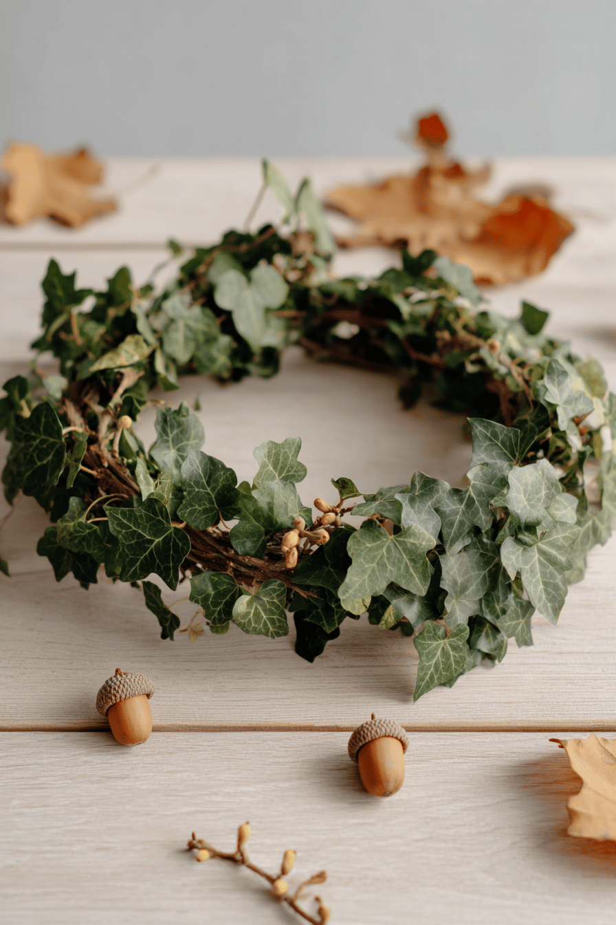 Ein schlichter Herbstkranz aus Efeu mit Eicheln auf hellem Holztisch