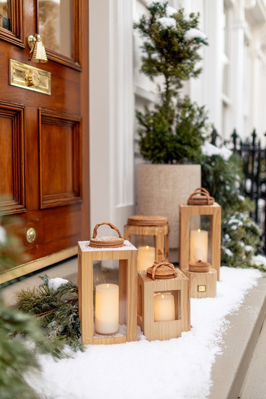 Verschneite Holzlaternen mit Kerzen vor einer Haustür, umgeben von Tannenzweigen