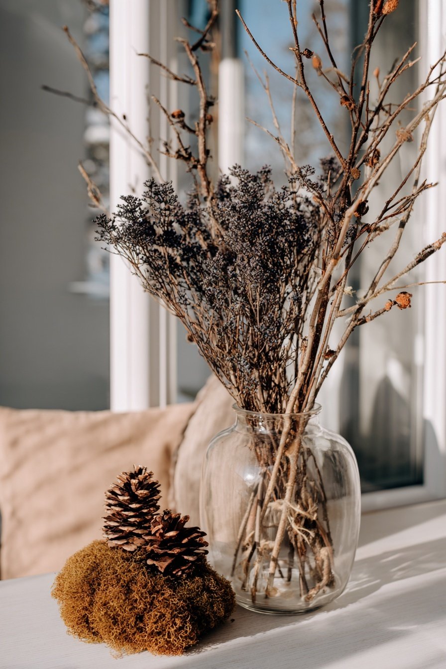 Trockene Zweige in einer Glasvase mit Zapfen und Moos dekoriert