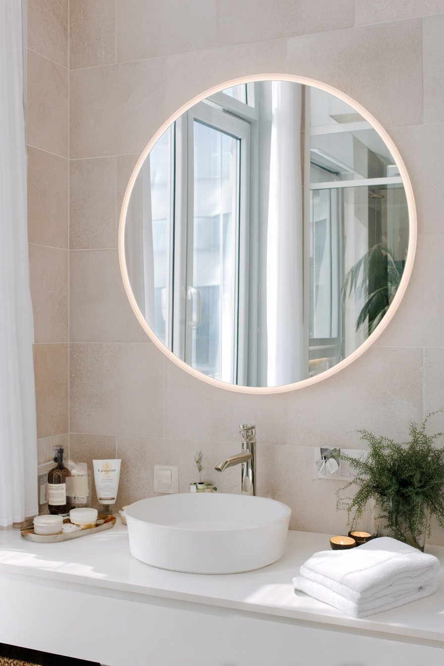 Modernes Gäste-WC mit rundem LED-Spiegel, Aufsatzwaschbecken und minimalistischer Deko